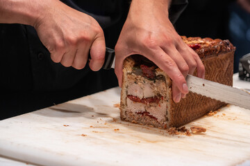 Male hand slicing with a big knife a pate en croute an appetizer  meat pie wrapped in hot water...