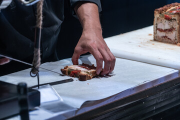 Male hand wrapping on a paper a pate en croute an appetizer  meat pie wrapped in hot water crust pastry at a French market. - obrazy, fototapety, plakaty