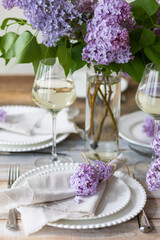 Beautiful table decor for a wedding dinner with a spring blooming lilac flowers. Celebration of a special event. Fancy white plates, wineglasses. Countryside style