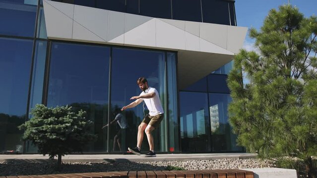 Pleasant sporty man doing squats exercises while training alone near building with glass wall. Confident active male warming up leg muscles before morning run.