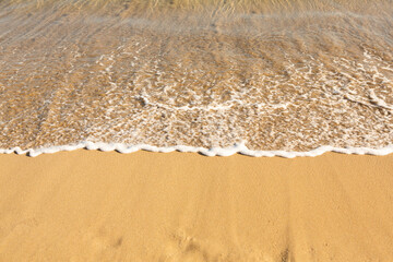 Background with golden sand on the coast of the island of Crete. Abstract surface with sand and clear sea water for text.