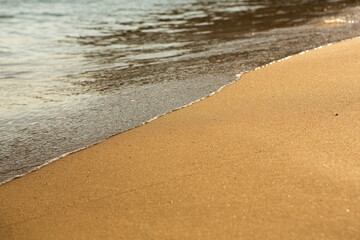 Background with golden sand on the coast of the island of Crete. Abstract surface with sand and clear sea water for text.