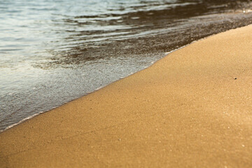 Background with golden sand on the coast of the island of Crete. Abstract surface with sand and clear sea water for text.