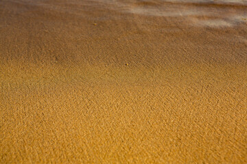 Background with golden sand on the coast of the island of Crete. Abstract surface with sand and clear sea water for text.