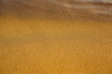 Background with golden sand on the coast of the island of Crete. Abstract surface with sand and clear sea water for text.