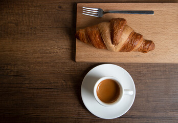 Croissant with espresso in white cup on wooden background
