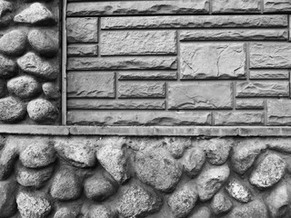 A fragment of a building wall with a facing material imitating natural stone, and with real boulders. Black and white monochrome photo.