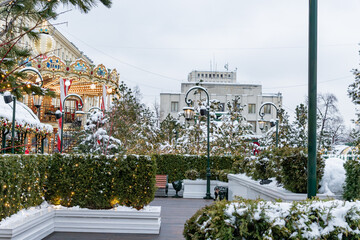 Festive Merry-go-round carousel in winter Square among christmas treees. Magic snowy cityscape.