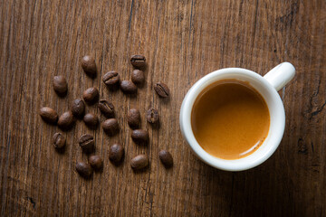 White cup of espresso with coffee beans on wooden background