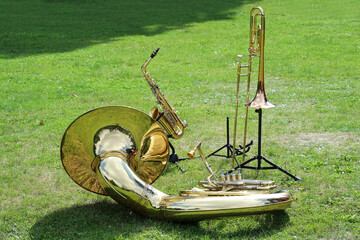 Various musical brass instruments like sousaphone, trombone and saxophone placed on the lawn and...