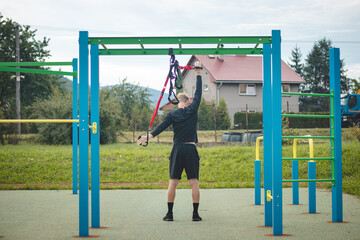 professional athlete stretches and strengthens his arms, shoulders, pectoral muscles and back muscles around the spine with Trx fitness straps. Support training for maximum performance