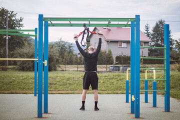 professional athlete stretches and strengthens his arms, shoulders, pectoral muscles and back muscles around the spine with Trx fitness straps. Support training for maximum performance