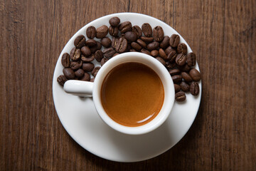 White cup of espresso with coffee beans on wooden background