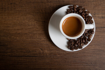 White cup of espresso with coffee beans on wooden background