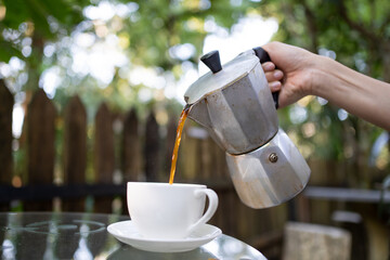 Lady hand pouring freshly brew coffee with Moka Pot with blur country side forest background....