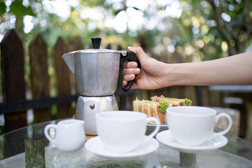 Lady hand holding Moka Pot with blur country side forest background. Morning brew coffee. Italian classic vintage coffee maker.