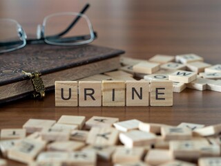 urine word or concept represented by wooden letter tiles on a wooden table with glasses and a book