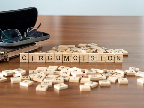circumcision word or concept represented by wooden letter tiles on a wooden table with glasses and a book