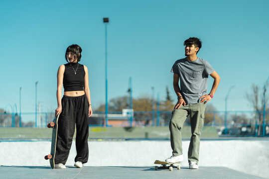 Couple of young skaters standing in the skate park with their skateboards and looking on the side