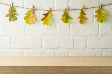 Empty wooden  table over brick wall and autumn leaves garland background. Autumn kitchen mock up for design and product display