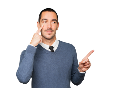 Hesitant young man making a gesture of being careful with his hand pointing at his eye