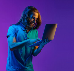 A nice emotional guy holds a laptop in his hands and looks at the screen with surprise. colored neon light
