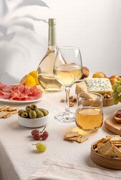 Glasses and bottle of white wine with grapes, cheese and salami on light table background. White wine with cheese and fruits. Wine bottle mockup with blank labels to place your design. Space for text