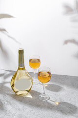 Glasses and bottle of white wine with blank label on light background. Wine making and wine degustation concept. Free space for your text