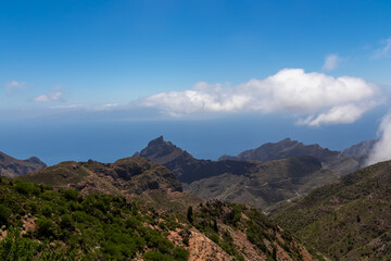 Fototapeta na wymiar Panoramic view on the Teno mountain massif seen from summit Pico Verde, Tenerife, Canary Islands, Spain, Europe. Hiking trail between Masca and Santiago. Clouds over lush green hills. Tropical climate
