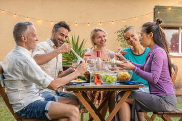 Happy family eating and drinking red wine at dinner barbecue outside. Mothers and youngsters eat...