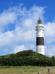 White lighthouse with a black stripe behind a meadow and houses in front of a cloudy sky on Sylt, Germany