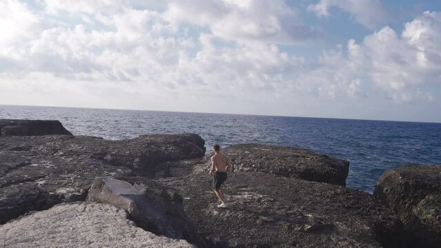 The man is running.
Adventurer man jogging dangerously on cliffs by the sea.
