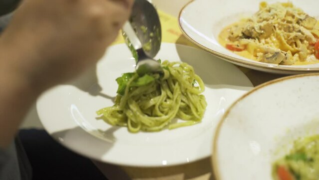 A woman puts pasta with a fork and spoon into a plate. Close-up.