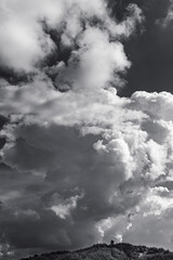 Obraz premium Black-and-white portrait format image of a landscape photographer looking tiny under a huge towering cumulus cloud