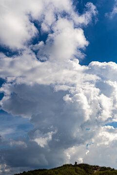 Portrait format image of a landscape photographer looking tiny under a huge towering cumulus cloud