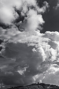 Black-and-white portrait format image of a landscape photographer looking tiny under a huge towering cumulus cloud