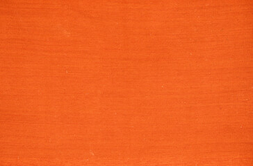 An old orange woven carpet in a solid color.