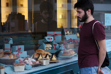 Young man choosing a pastry standing in front of bakery showcase.