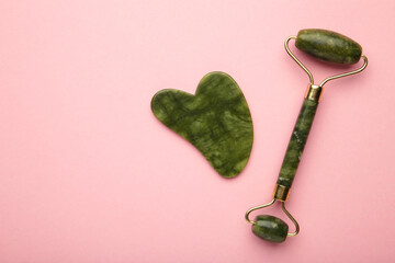 Green jade roller and gua sha stone for facial massage and on pink background. Home beauty and selfcare accessories. Face roller for anti age wrinkle treatment. Top view, flat lay. © Mouse family