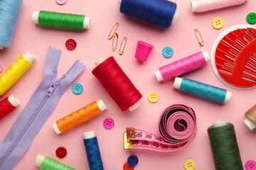 Fototapeta na wymiar Sewing supplies on pink background: sewing thread, scissors, a large spool of thread, pieces of cloth, needles,centimeter, buttons