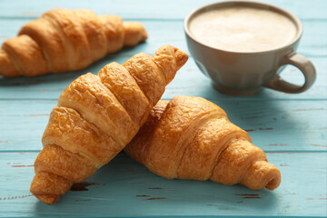 French croissants and cup of coffee on blue wooden background.