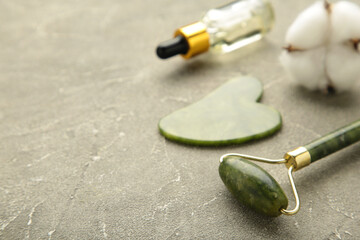 Green jade roller and gua sha stone for facial massage and on grey background. Home beauty and selfcare accessories. Face roller for anti age wrinkle treatment. Top view, flat lay.