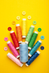 Colorful buttons with colorful thread on yellow background. Vertical photo