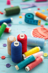 Sewing supplies on blue background: sewing thread, scissors, a large spool of thread, pieces of cloth, needles,centimeter, buttons. Vertical photo