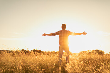 Happy person in the field at sunset. Young man feeling free energized in nature. - obrazy, fototapety, plakaty
