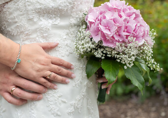 Hände vom Brautpaar mit Eheringen auf Brautstrauß am Hochzeitstag als close-up