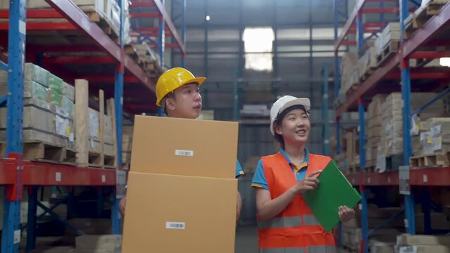 4K, Slow motion, Two Asian male and female workers, checking boxes inside the warehouse, two walking and talking about work, both wearing helmets and reflective green shirts for their own safety.