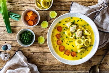 Bowl of hot leek soup with chicken meat on wooden table
