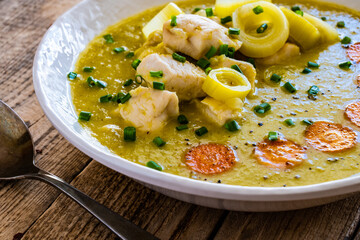 Bowl of hot leek soup with chicken meat on wooden table
