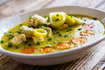 Bowl of hot leek soup with chicken meat on wooden table
